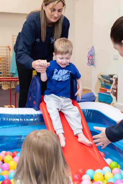 A child enjoying a slide into a ball pool with support from the Little Discoverers team.