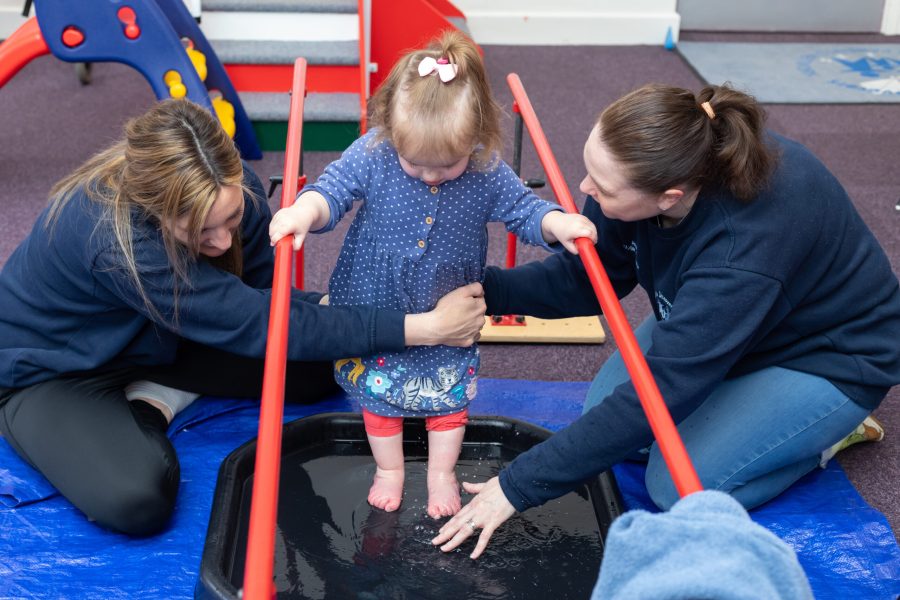 A child taking part in a supported water-play activity with two members of the Little Discoverers team.